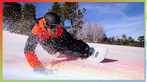 Snowboarder in black and orange jacket with black helmet carving the slopes with right hand dragging on snow.